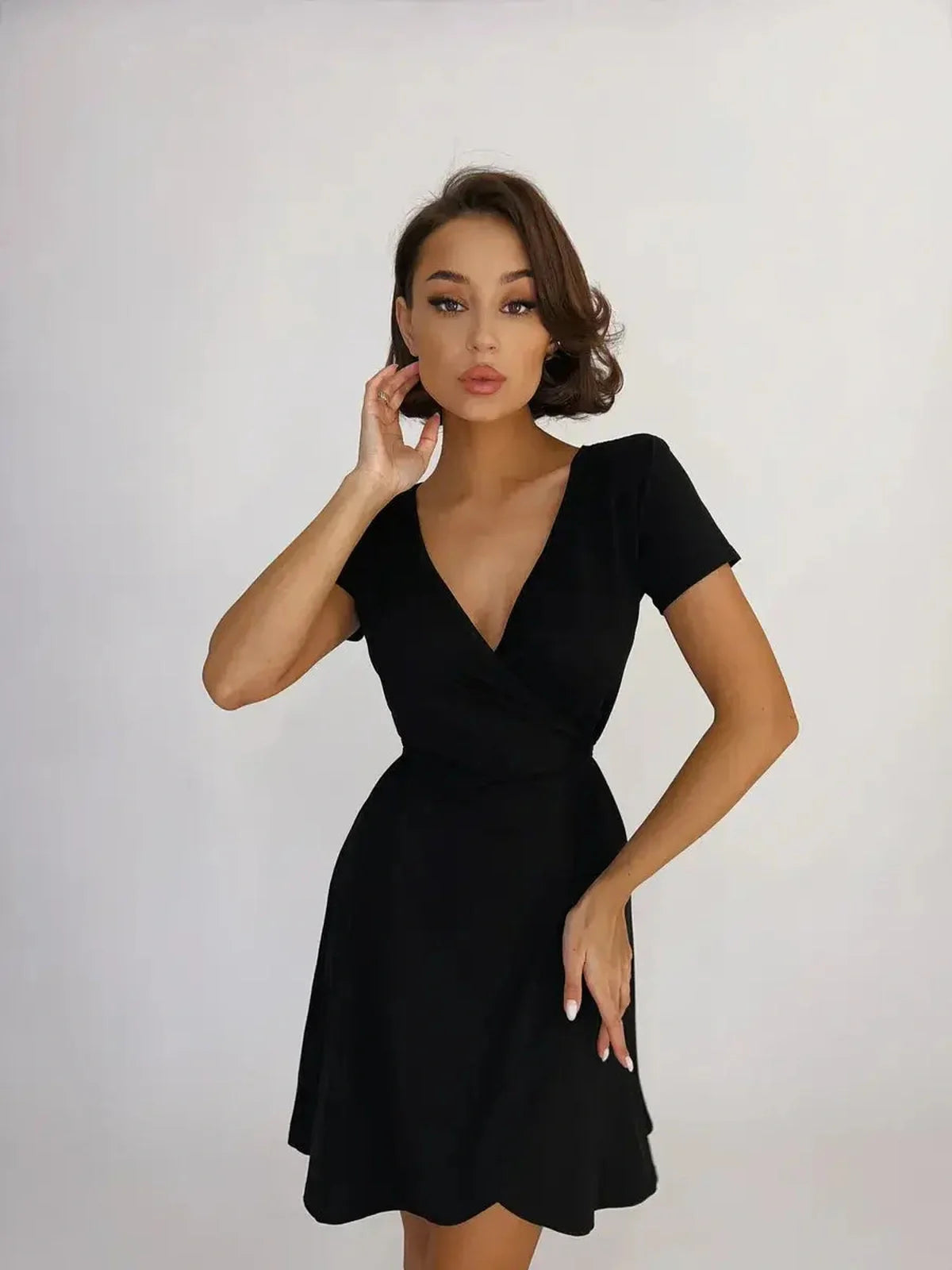 Model showcasing a sleek black mini dress with a deep V-neckline and fitted wrap design.
