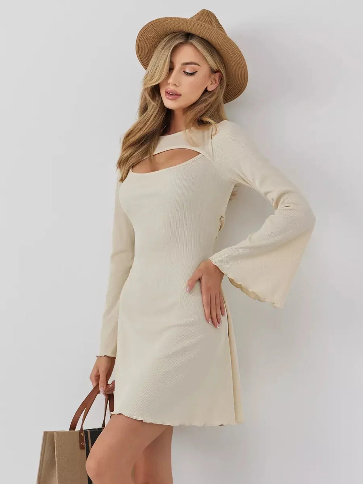 Model wearing the Sculpted Grace mini dress with long sleeves and a front cutout, styled with a hat and tote bag.