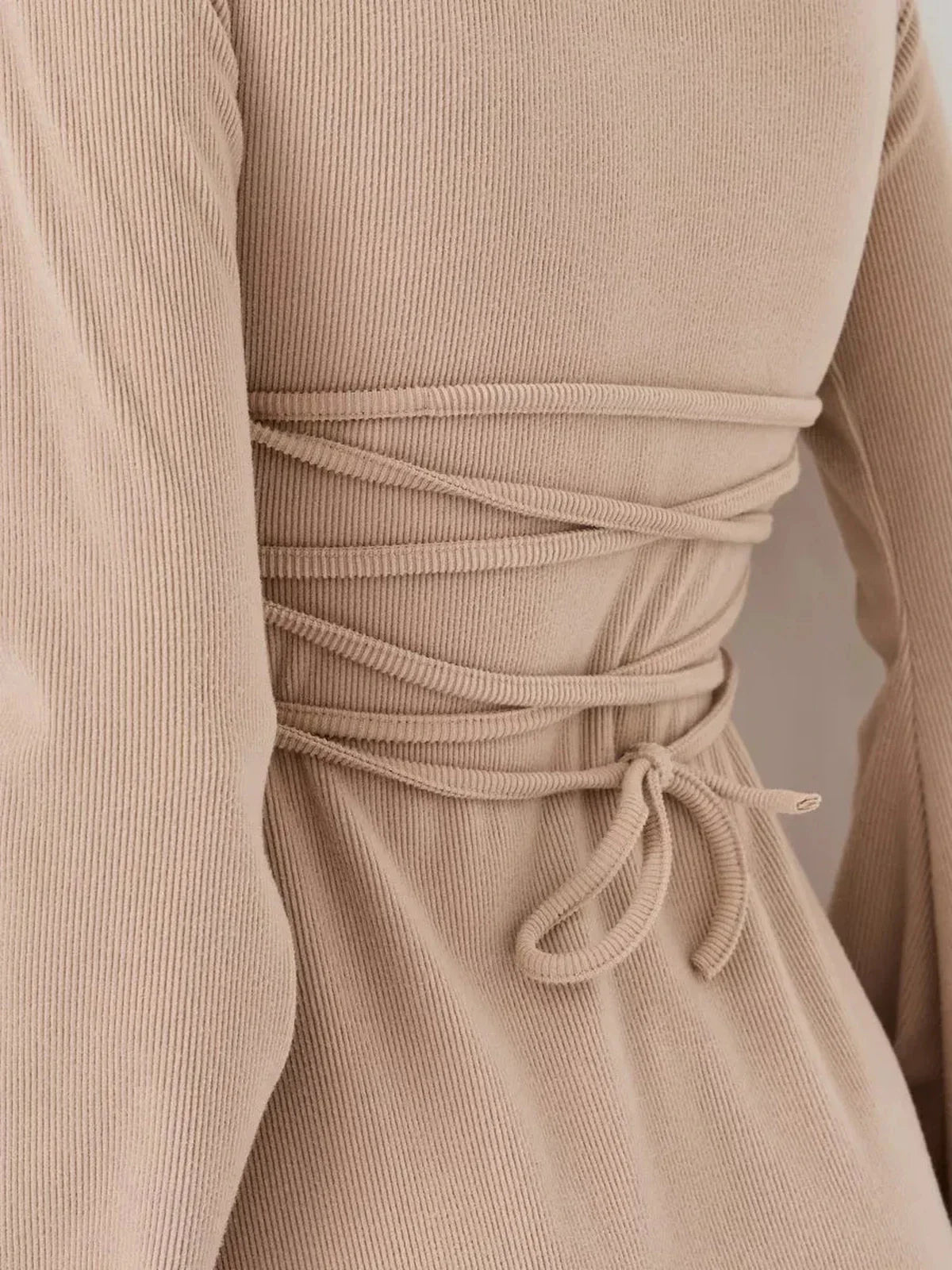 Close-up of the back of a beige ribbed mini dress showcasing its stylish lace-up design and fitted silhouette.