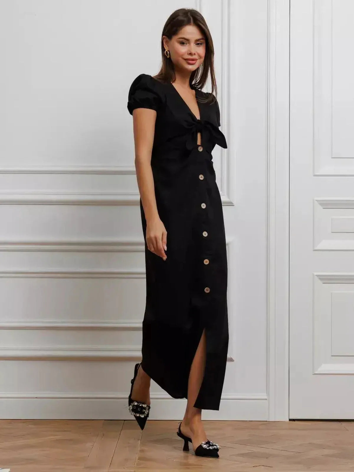 Elegant black maxi dress with tie-front detail, puff sleeves, and contrast buttons, showcasing contemporary femininity.