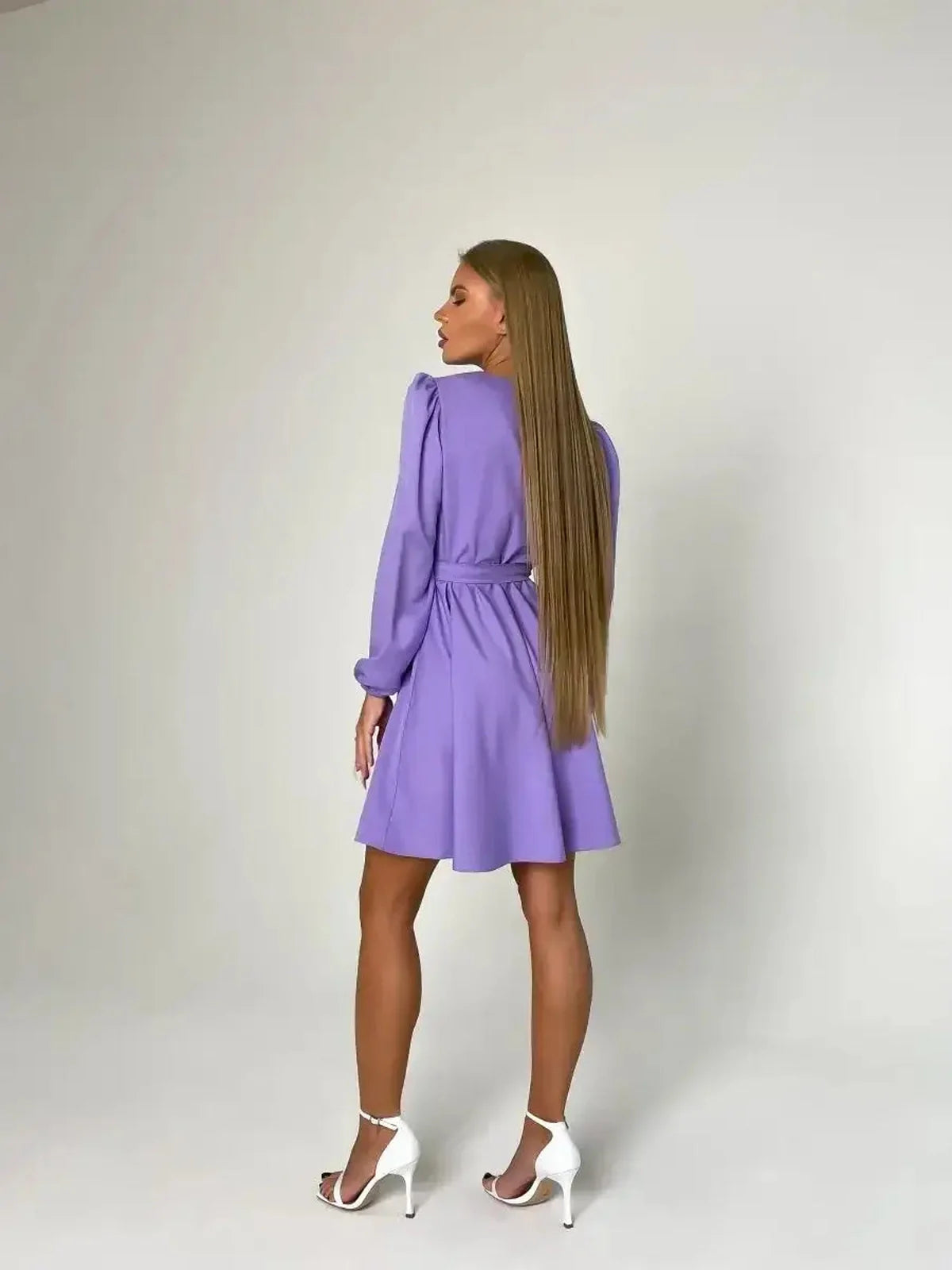 Back view of a woman in a tailored lilac mini dress with long sleeves and a cinched waist, exuding elegance.