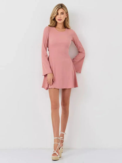 Model wearing the Blush Aura mini dress, a pink A-line dress with long flared sleeves, perfect for summer elegance.