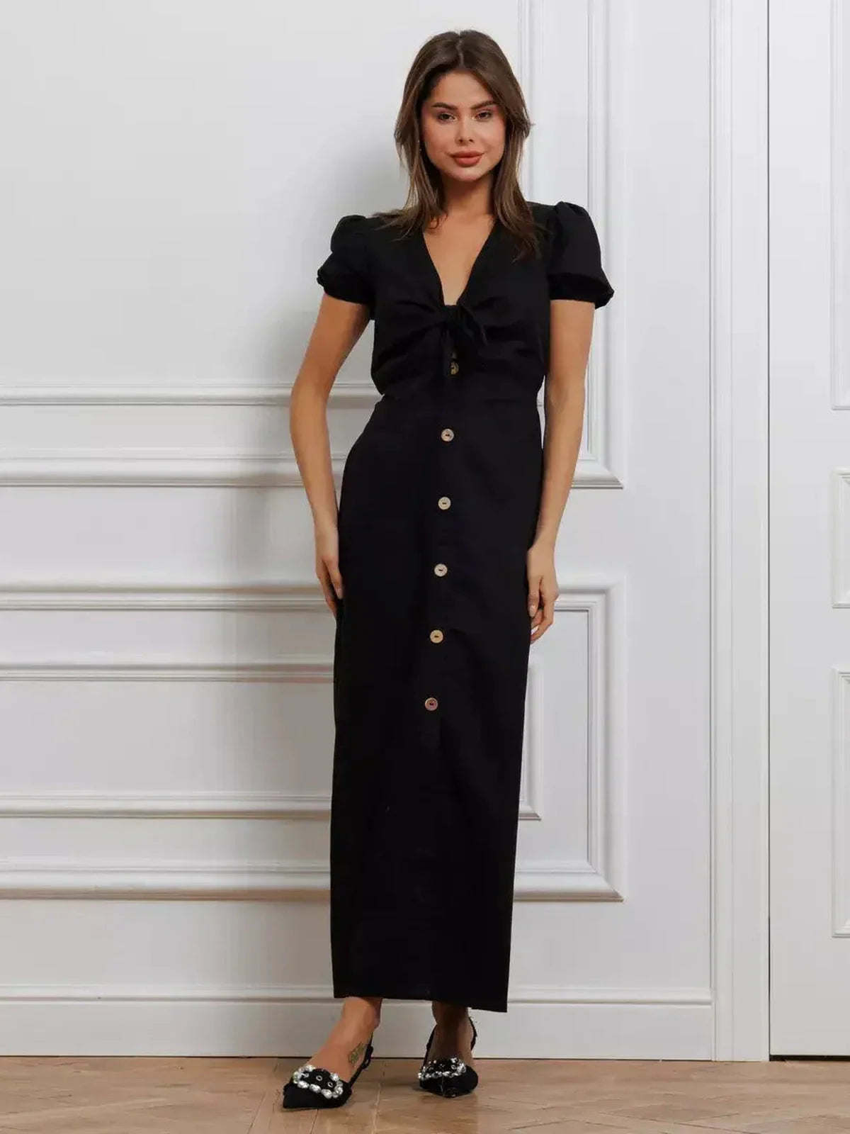 Model wearing the Maxi Dress Noir Belle, featuring a tie-front detail and contrast buttons, showcasing elegance and femininity.