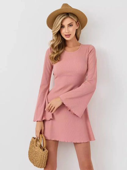 Woman in a blush mini dress with flared sleeves and a U-neckline, accessorized with a straw hat and handbag.