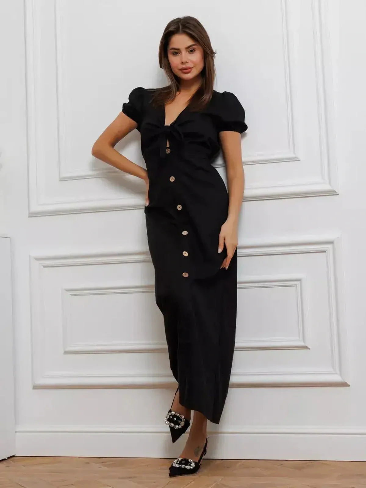 Elegant black maxi dress with tie-front detail and contrast buttons, featuring puff sleeves and a flattering V-neckline.