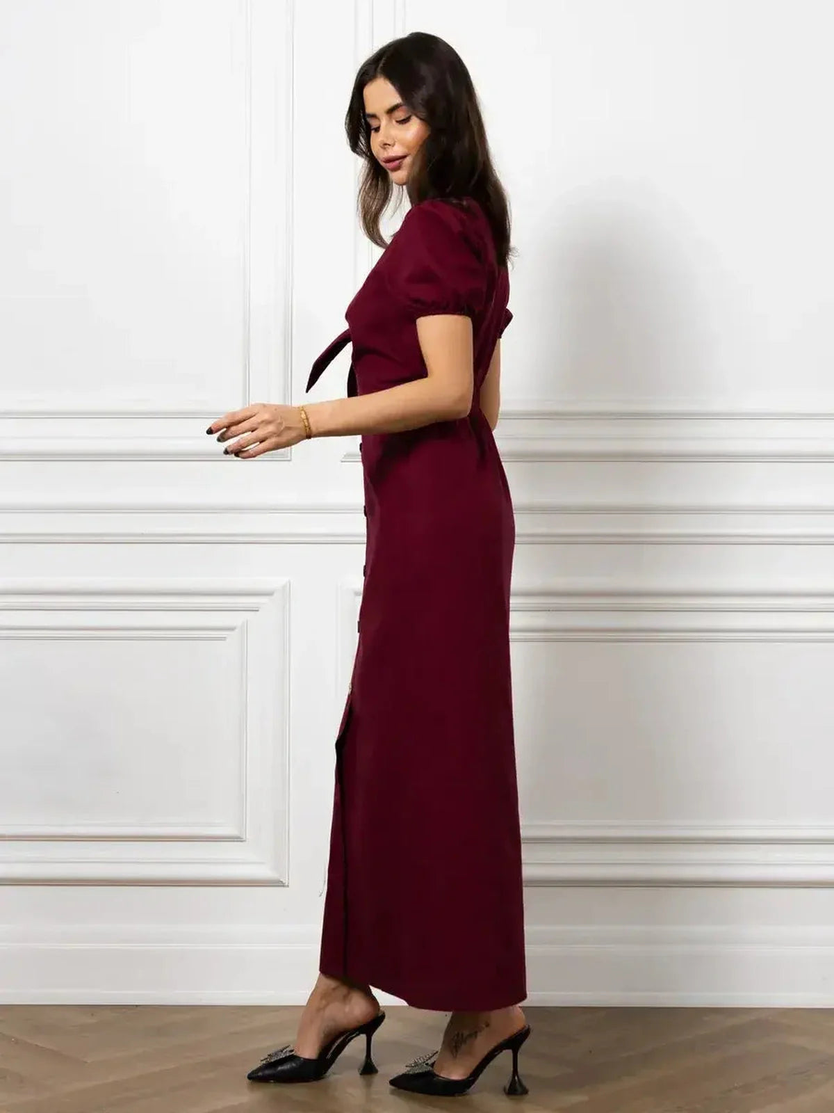 Model showcasing the Maxi Dress Merlot Grace in burgundy, featuring a front bow and structured puff sleeves.