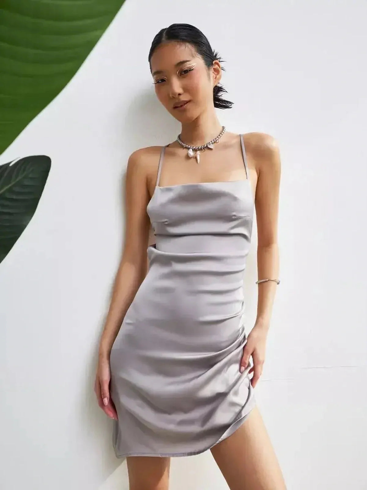 Model showcasing the Silken Rush mini dress in silver-gray with satin effect and crisscross tie straps, perfect for summer soirées.