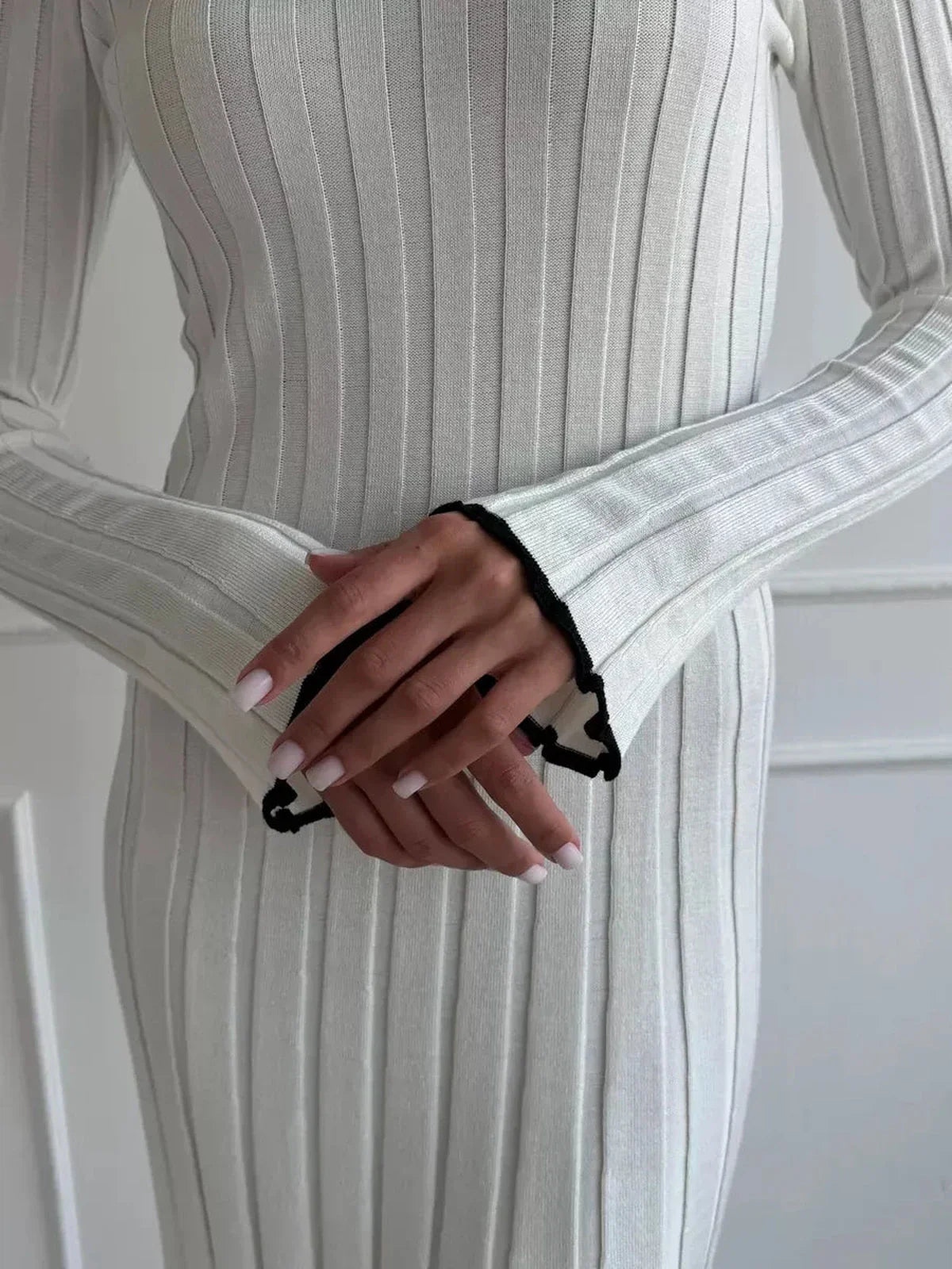 Close-up of hands in an ivory ribbed knit maxi dress showcasing elegant ruffle cuff details and chic style.