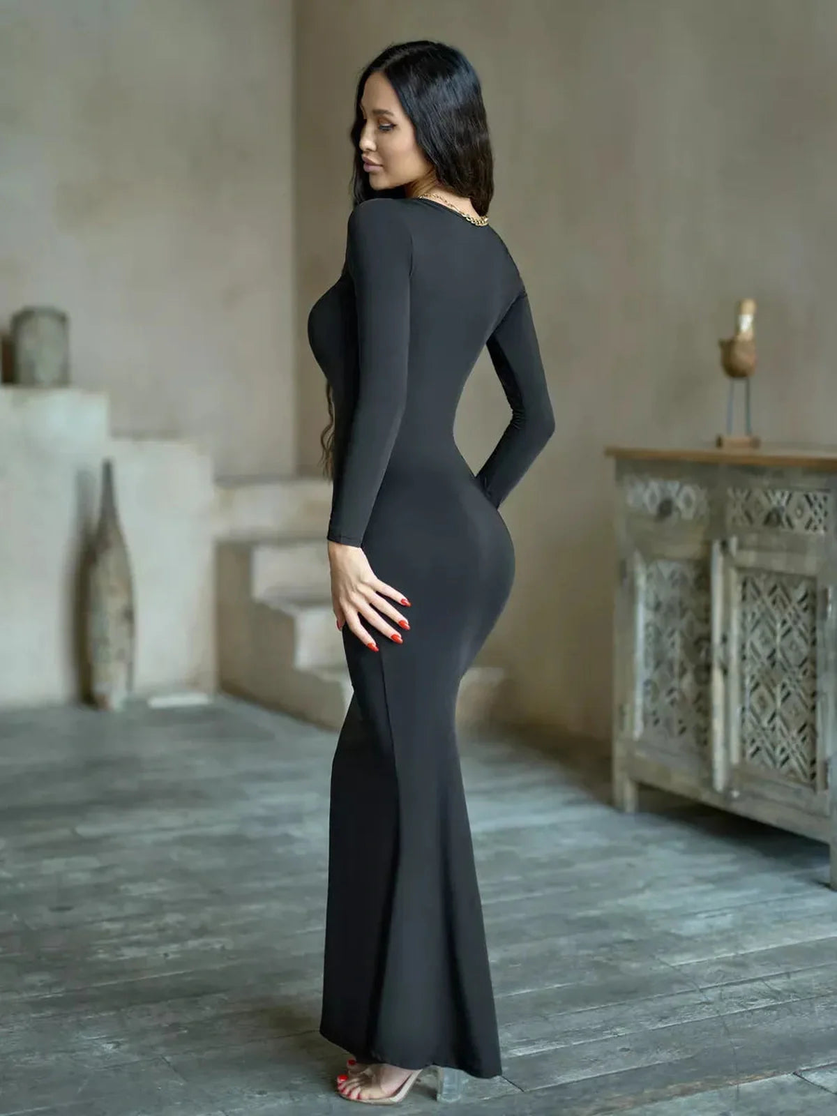 Side view of a model wearing the Sculpted Noir Maxi Dress, showcasing its sleek silhouette and long sleeves.