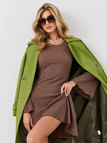 Model in a Flare Hour Mini dress featuring bell sleeves and a flared hem, paired with a chic green coat and stylish sunglasses.