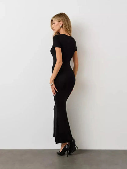 Elegantly styled woman in a Noir Curve Maxi Dress showcasing its sculpted silhouette and flared hem against a minimalist backdrop.