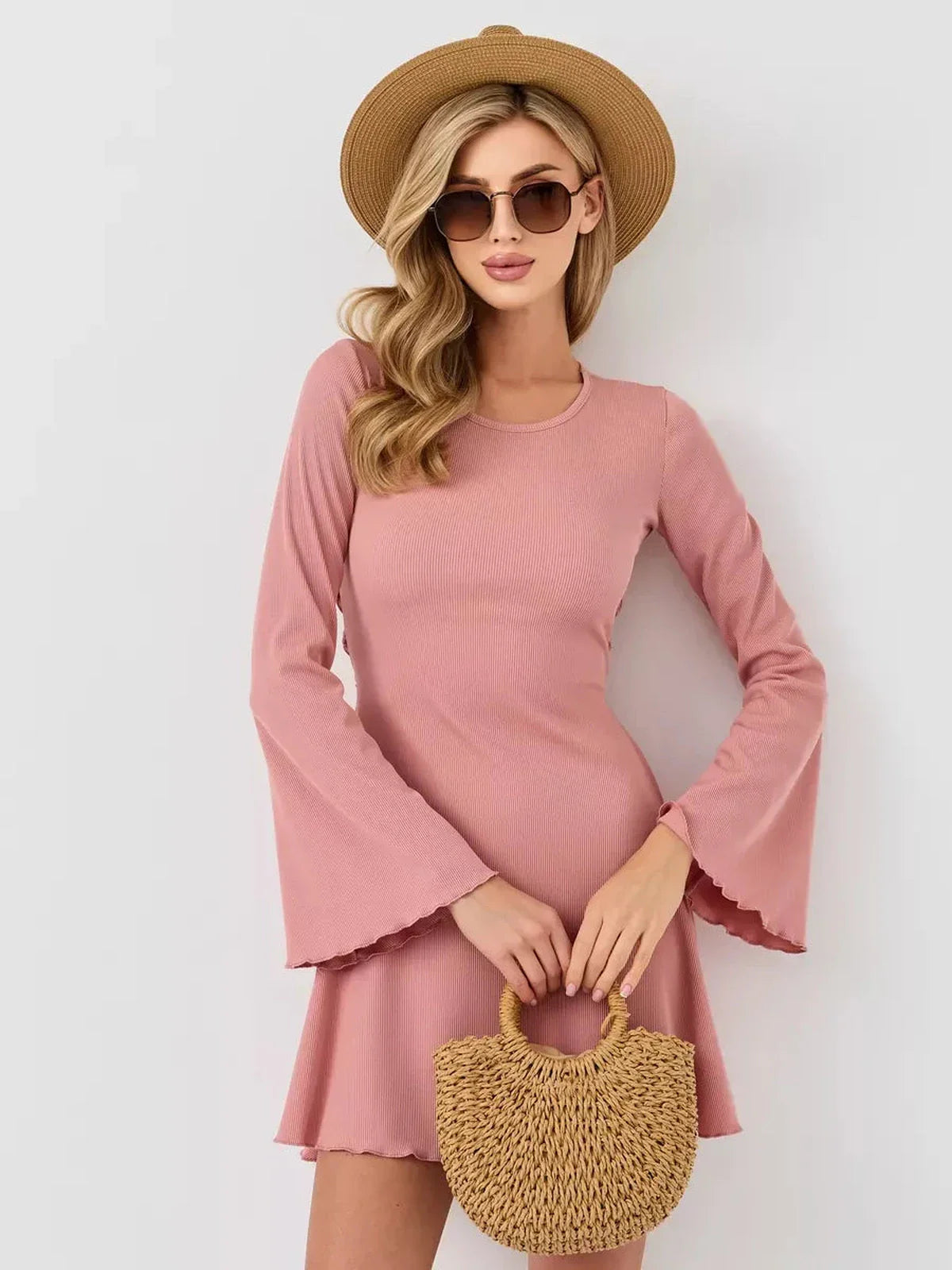 Model wearing a chic Blush Aura mini dress with flared sleeves, a U-neckline, and a stylish straw hat and bag.