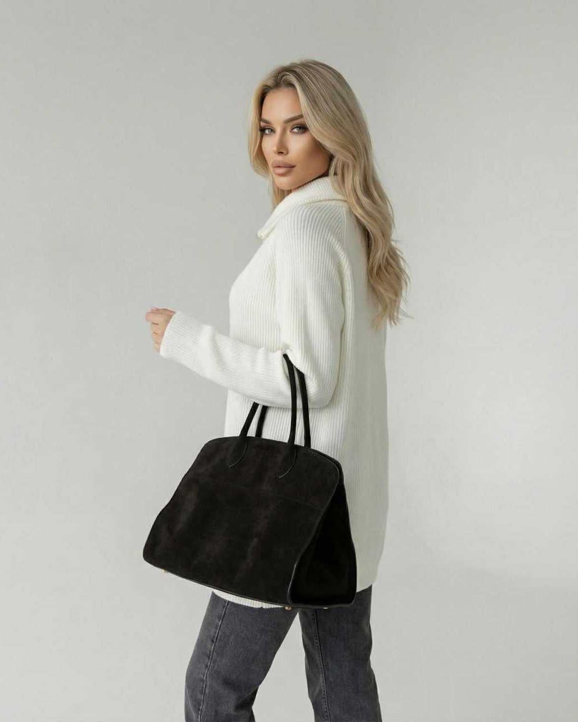 Woman wearing a white Aspen Sweater, holding a black tote bag, showcasing a chic look.