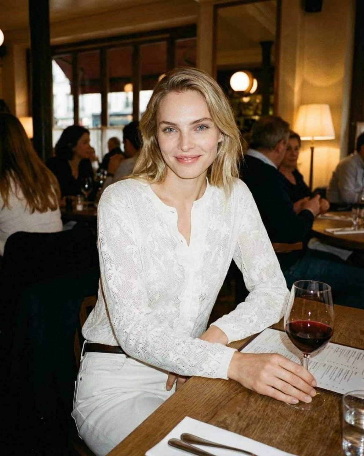 Elegant woman wearing the Monaco Blouse by Lauven, enjoying a glass of wine in a stylish restaurant setting.