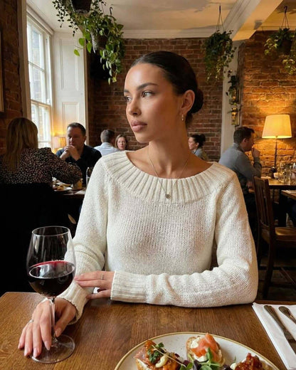 Sienna Sweater worn by a woman in a cozy restaurant setting, featuring a boat neck silhouette and rib knit detail.