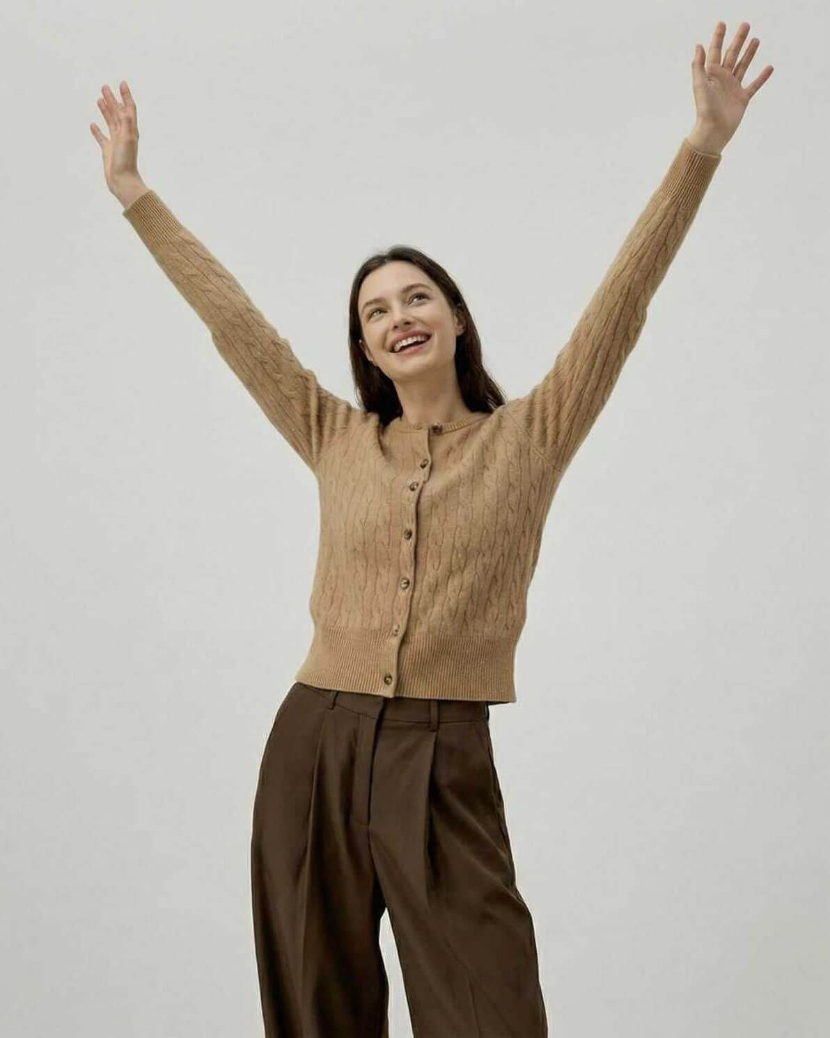 Happy woman wearing the Sienna Cardigan by Lauven, showcasing its classic cable knit design.