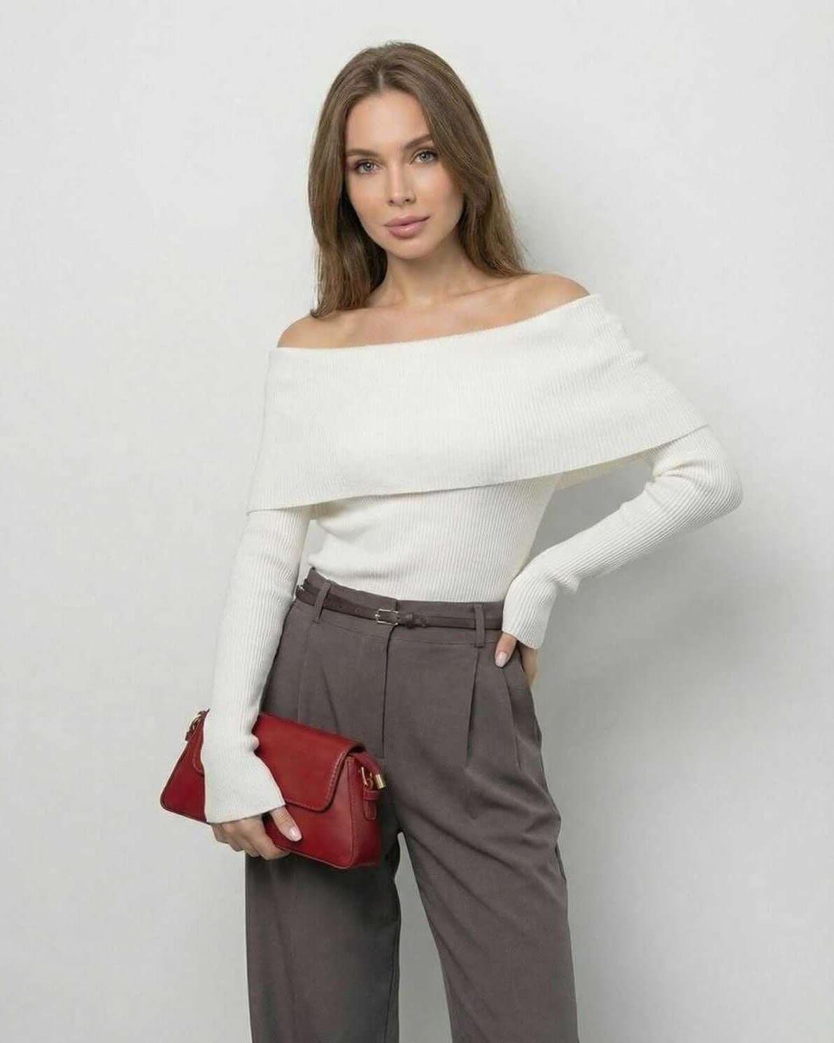 Model wearing the Milano Top by Lauven, an off-the-shoulder long sleeve top in solid white, paired with chic grey trousers.
