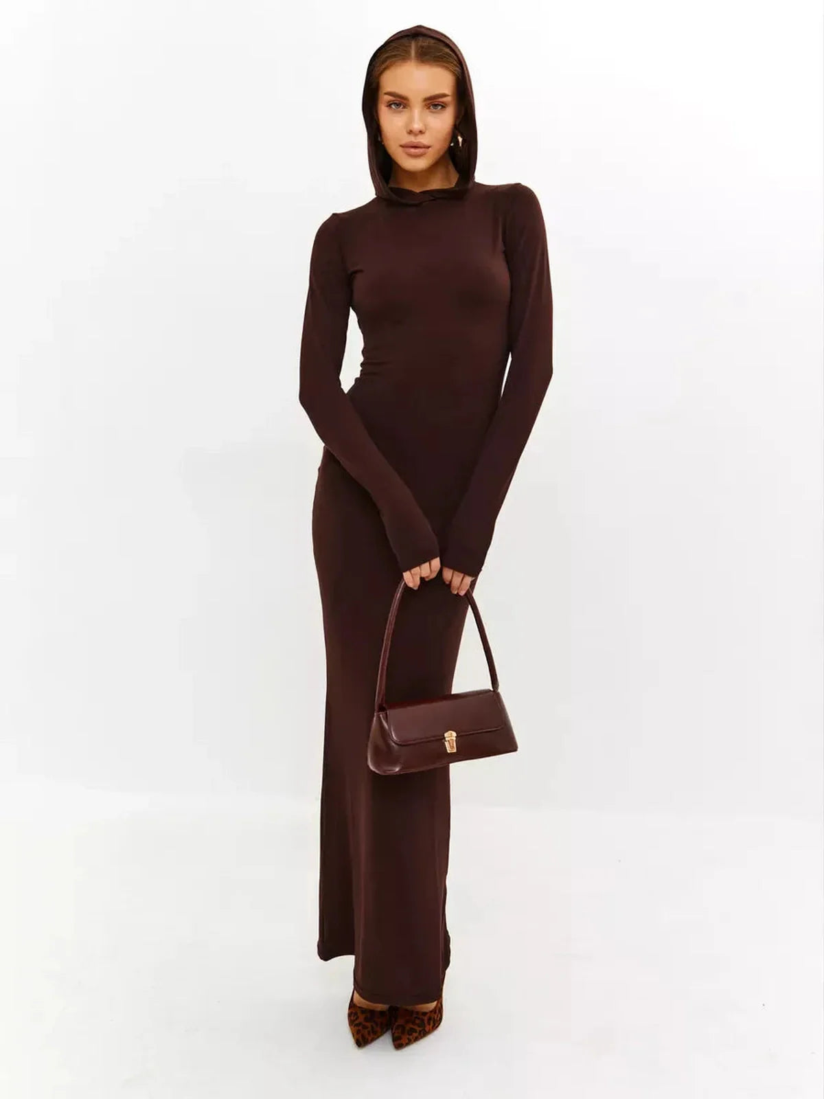 Model wearing Sculpt Maxi Dress in rich chocolate, showcasing hooded design and sleek silhouette with stylish handbag.