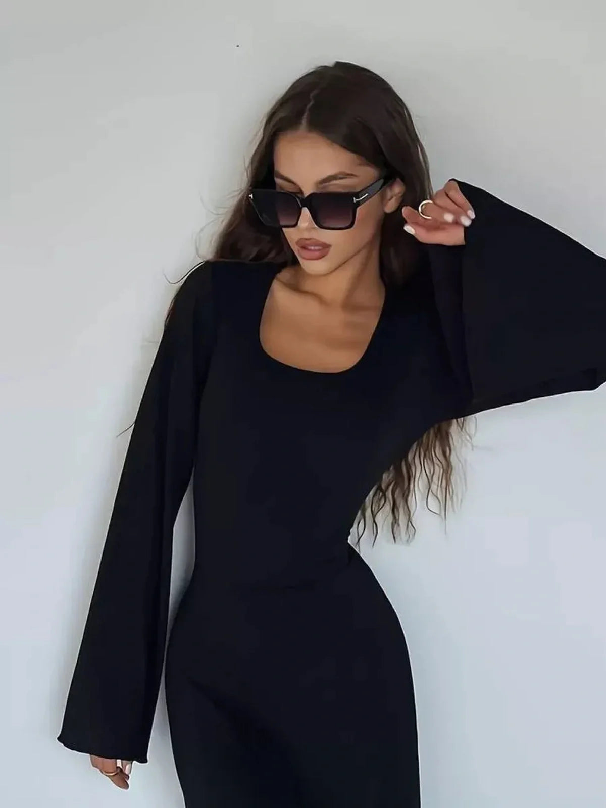 Woman in a noir contour maxi dress with flared sleeves and sunglasses against a simple background.
