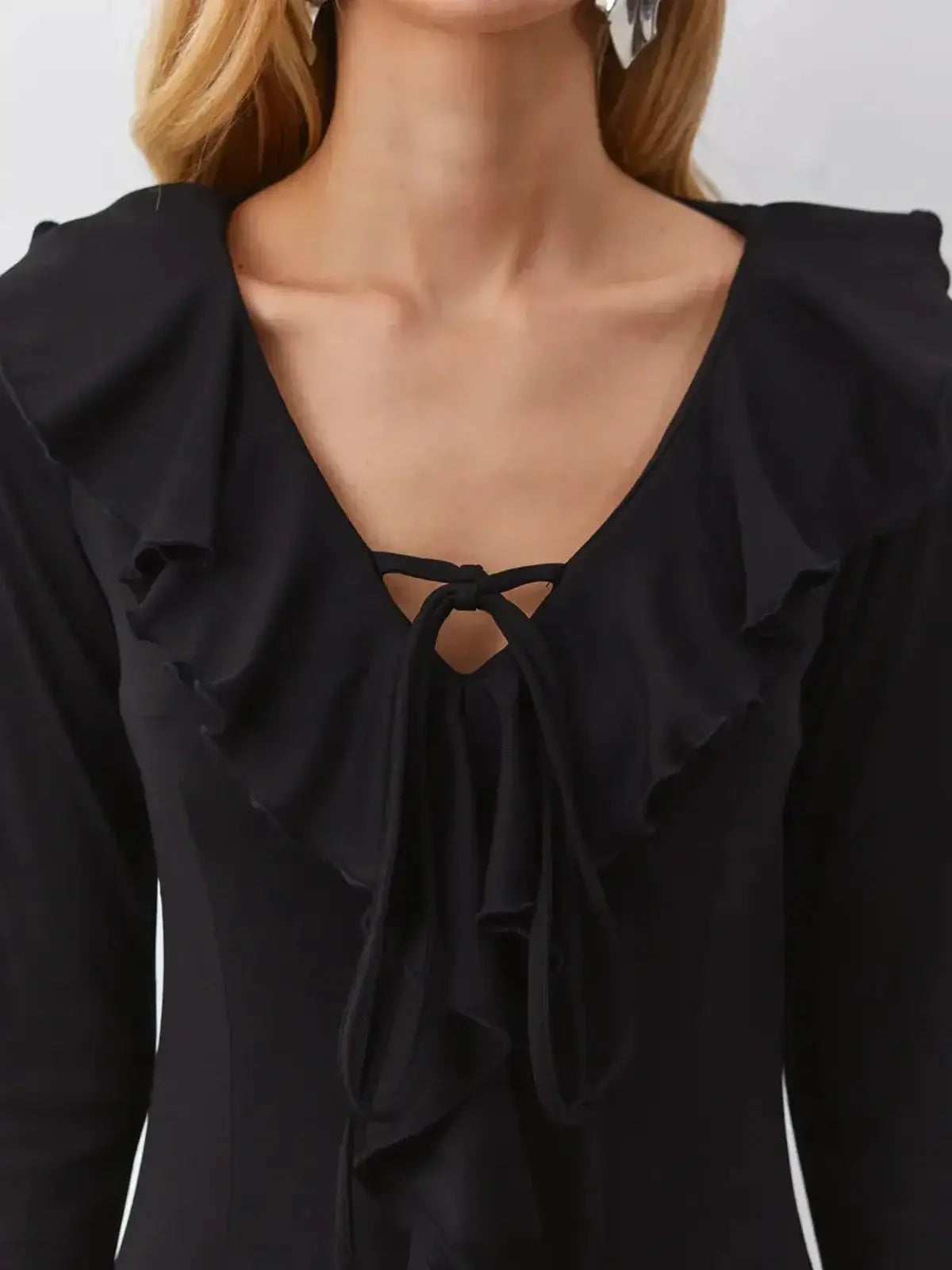Close-up of the Velvet Noir black dress featuring a V-neckline and ruffled detailing for a feminine look.