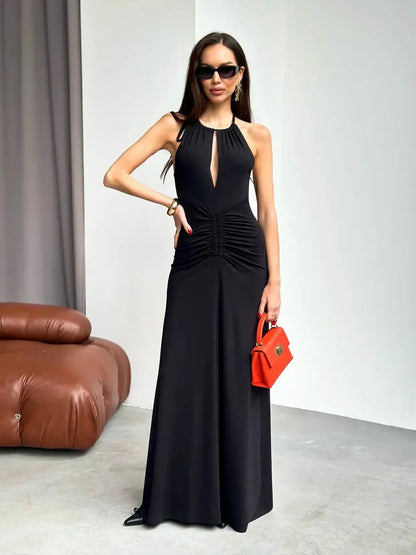 Elegant black halter maxi dress with front keyhole cutout and ruched detail, complemented by an orange handbag.