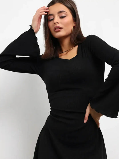 Model wearing a stylish black mini dress with flared long sleeves and a U-neckline, showcasing elegance and confidence.