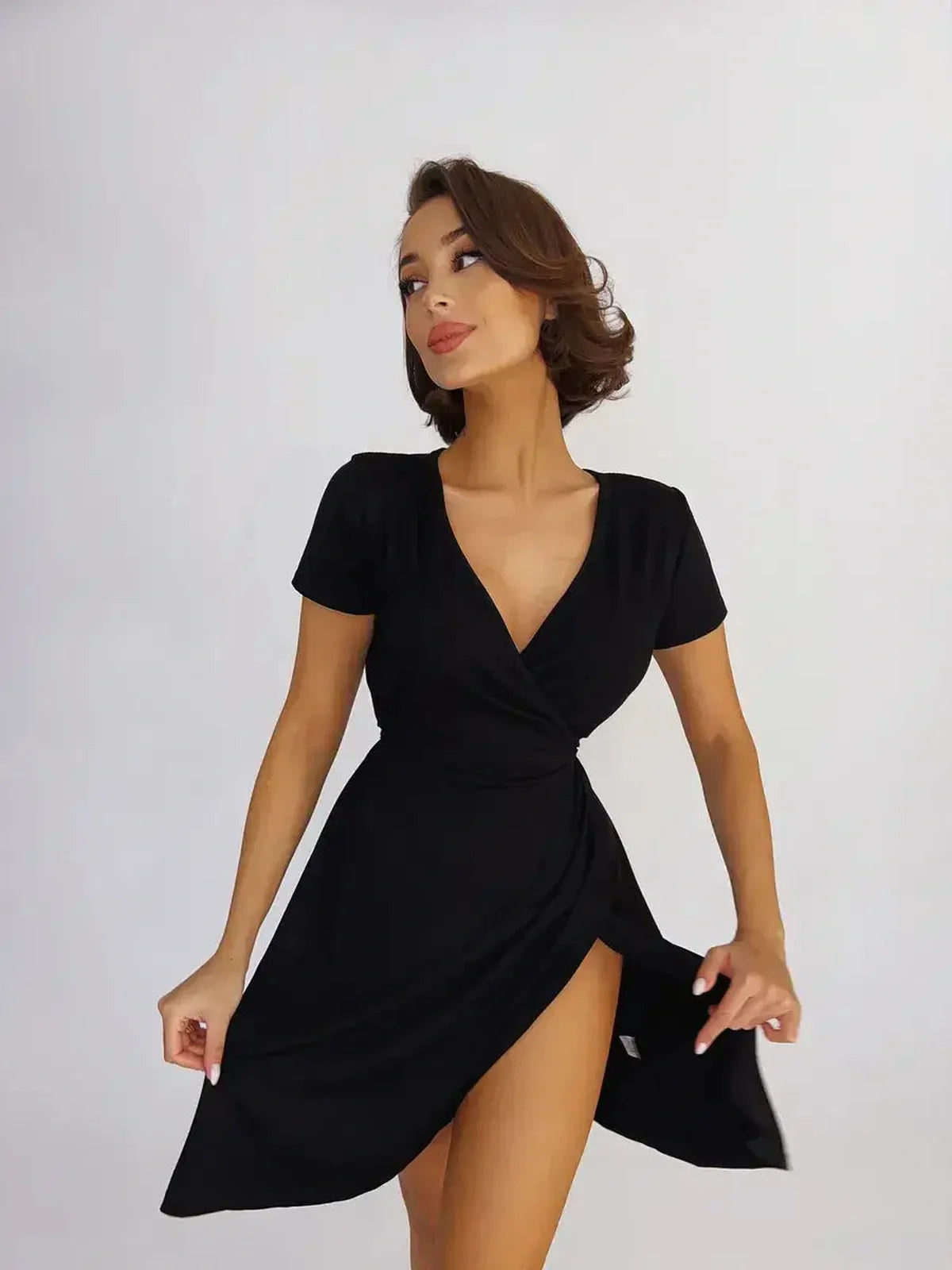 Model showcasing the Velvet Hour black mini dress with a fitted wrap design and deep V-neckline.