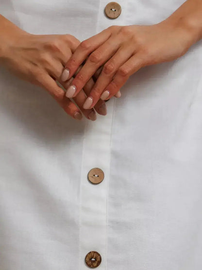 Close-up of hands holding the button-down front of a white maxi dress with natural wooden buttons.