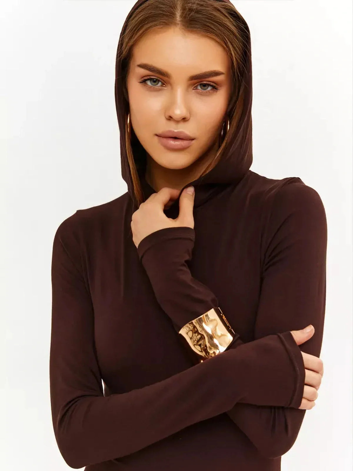 Woman wearing a hooded Sculpt Maxi Dress in chocolate brown, showcasing a sleek silhouette and stylish gold-accented sleeve.