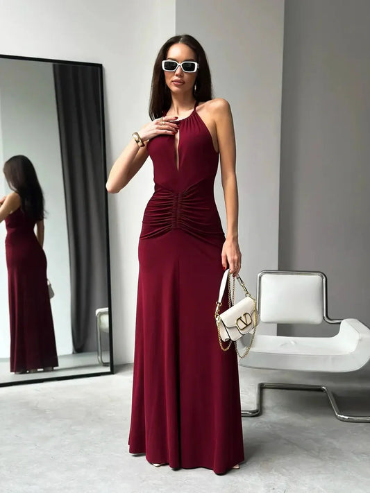Model wearing Maxi Dress Élan, a burgundy halter design with ruched waist and keyhole detail, in a chic indoor setting.