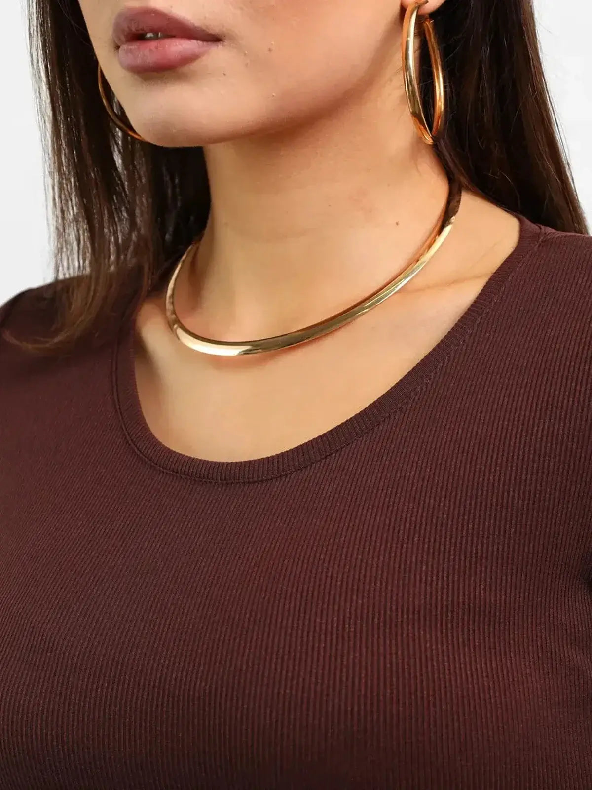 Close-up of a woman wearing a brown ribbed top, showcasing gold hoop earrings and a sleek gold necklace.