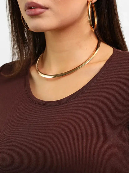 Close-up of a woman wearing a brown ribbed top, showcasing gold hoop earrings and a sleek gold necklace.