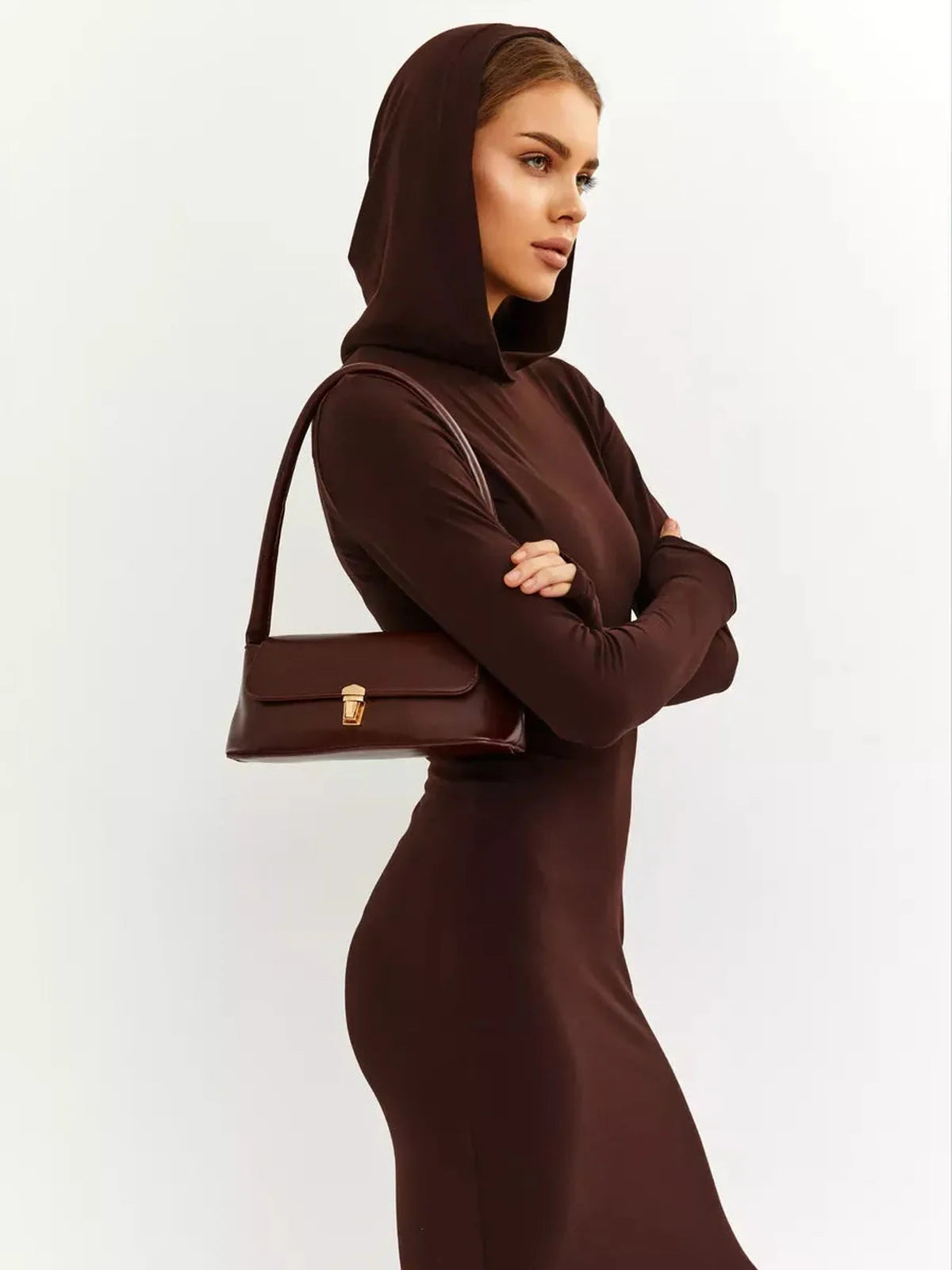 Model showcasing the Sculpt Maxi Dress in rich chocolate, featuring a hood and a sleek silhouette, paired with a stylish handbag.