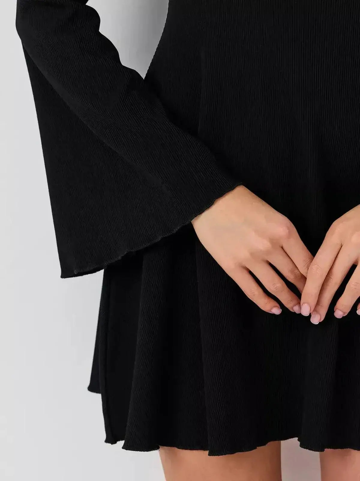 Close-up of a model's hands showcasing the flared cuffs and skirt of a black Velvet Hour mini dress.