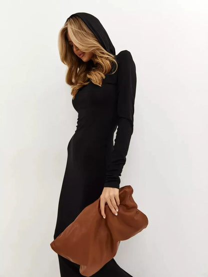 Chic woman in Noir Maxi Dress with hood, holding a brown clutch, showcasing minimalist urban elegance.