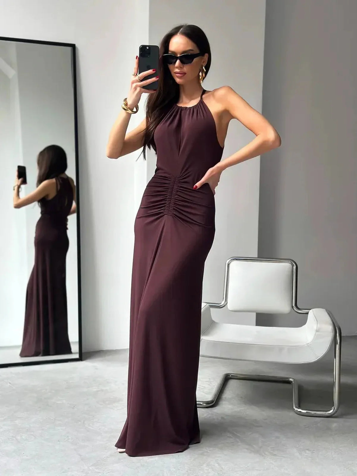 Model showcasing the elegant Maxi Dress Sienna with halter neckline and ruched details against a modern backdrop.