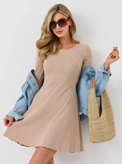 Woman modeling a warm beige ribbed mini dress with long bell sleeves and a denim jacket, paired with sunglasses.