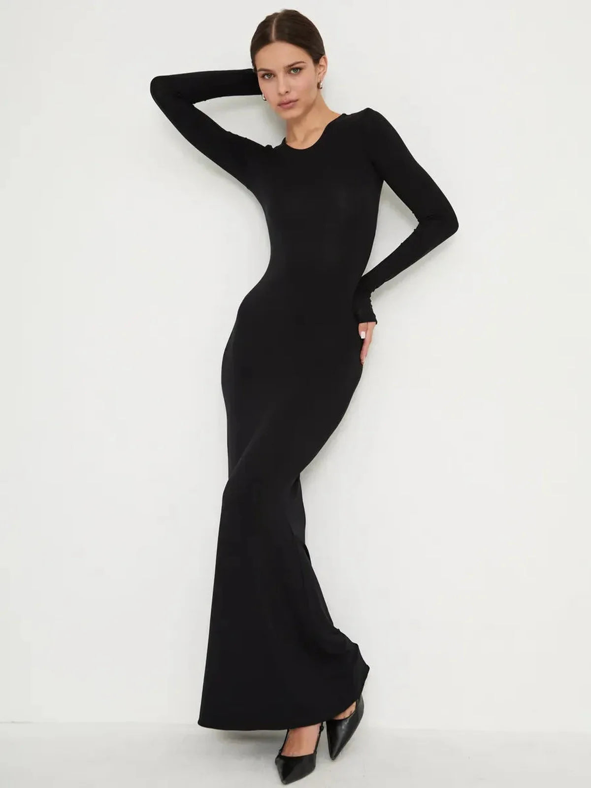 Model wearing Sculpted Noir full-length black dress, featuring long sleeves and a mermaid-style hem for elegant minimalism.