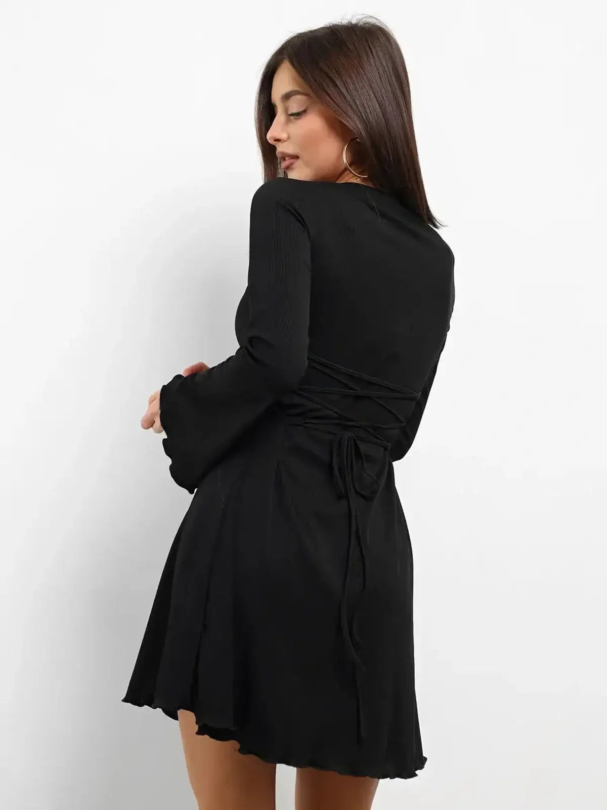 Model showcasing the back of the Noir Laced black mini dress with lace-up detail and flared sleeves.