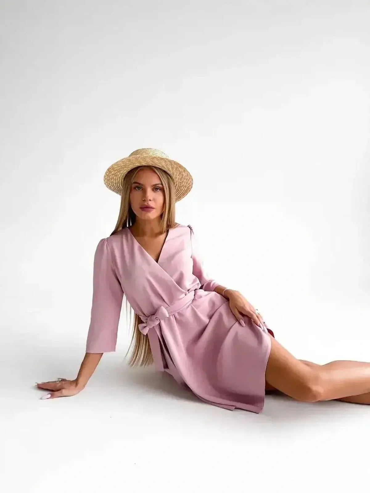 Model showcasing the Rosé Flair pink mini dress with long sleeves and removable belt, styled with a straw hat.