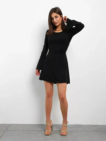 Model wearing Noir Laced black mini dress with flared long sleeves and U-neckline, perfect for parties or weddings.