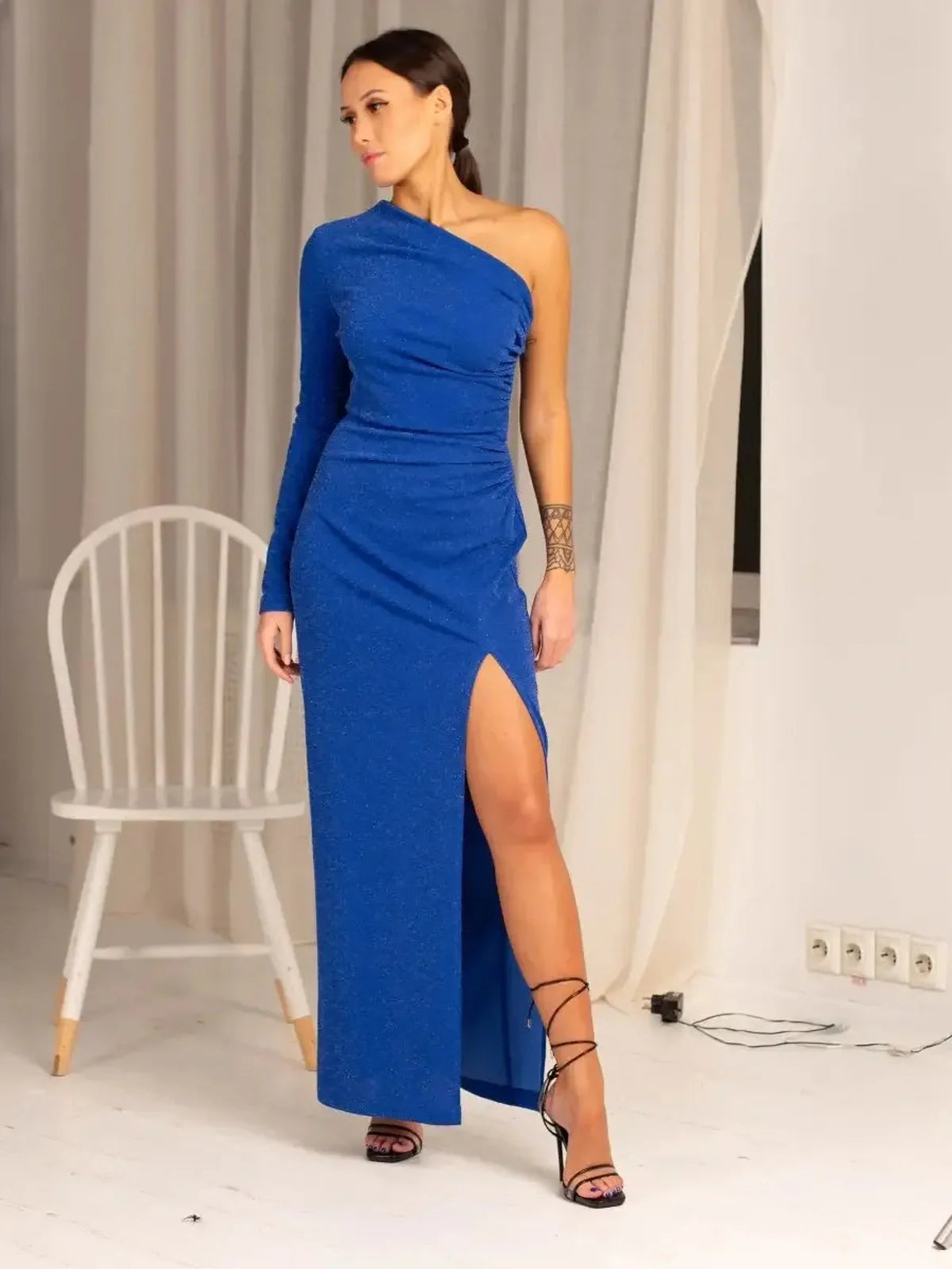 Woman in a striking sapphire one-shoulder maxi dress with a thigh-high slit, showcasing elegance and allure.