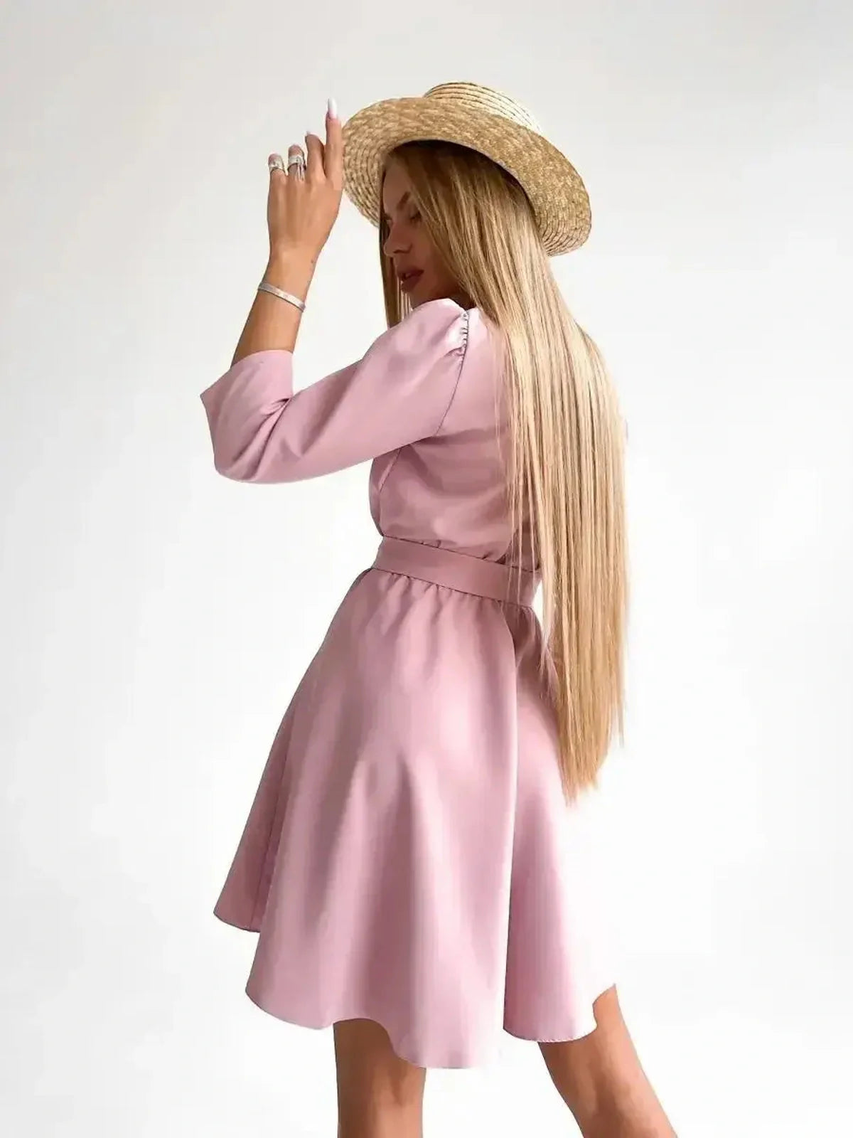Model wearing the Rosé Flair pink mini dress with long sleeves and a removable belt, styled with a straw hat.