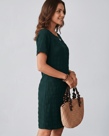 Avelin Mini Dress in textured fabric with round neckline, short sleeves, styled with a straw bag. Lauven brand.