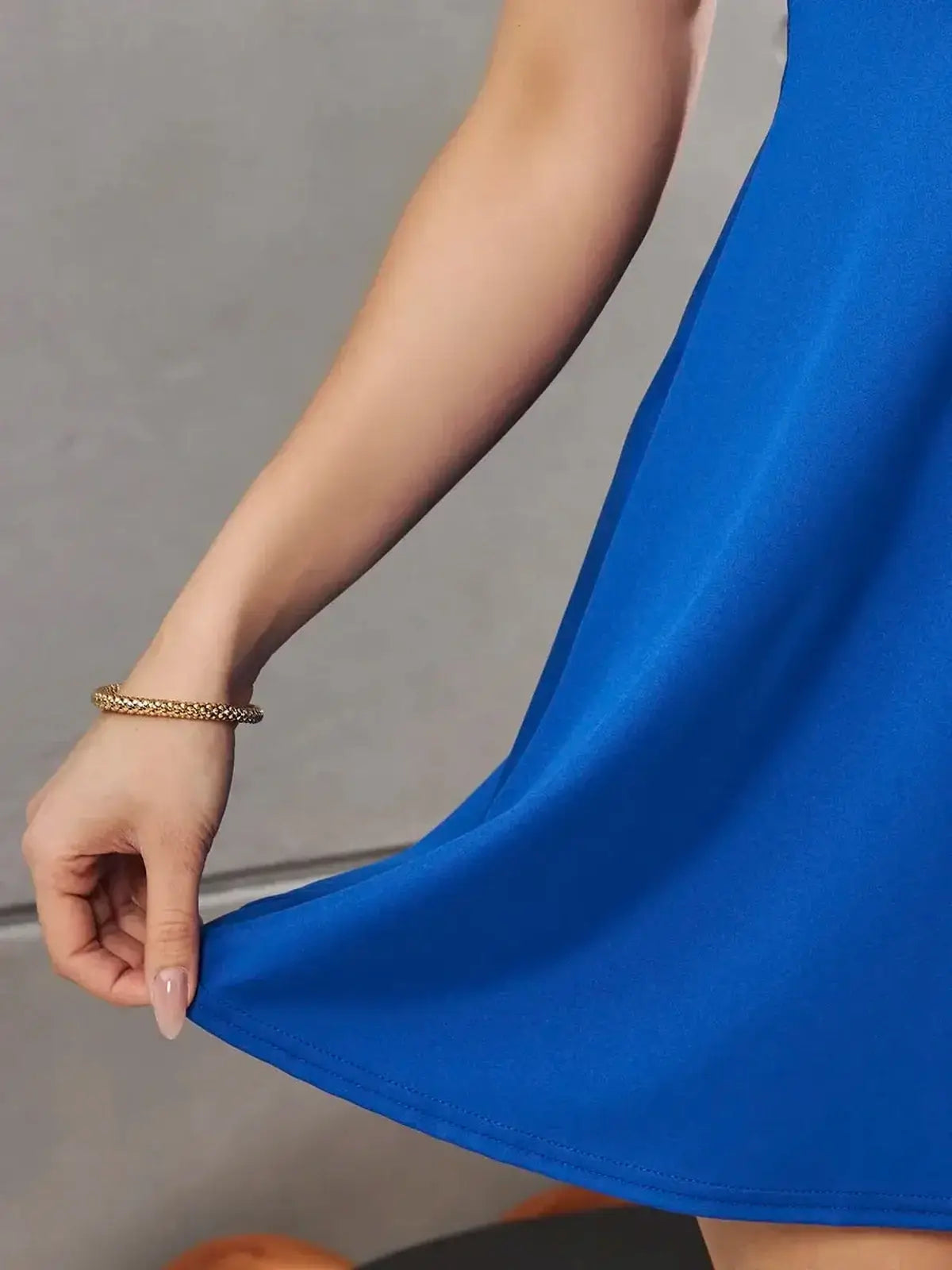 Close-up of a woman holding the hem of a vibrant blue mini dress, showcasing its flowy fabric and elegant silhouette.
