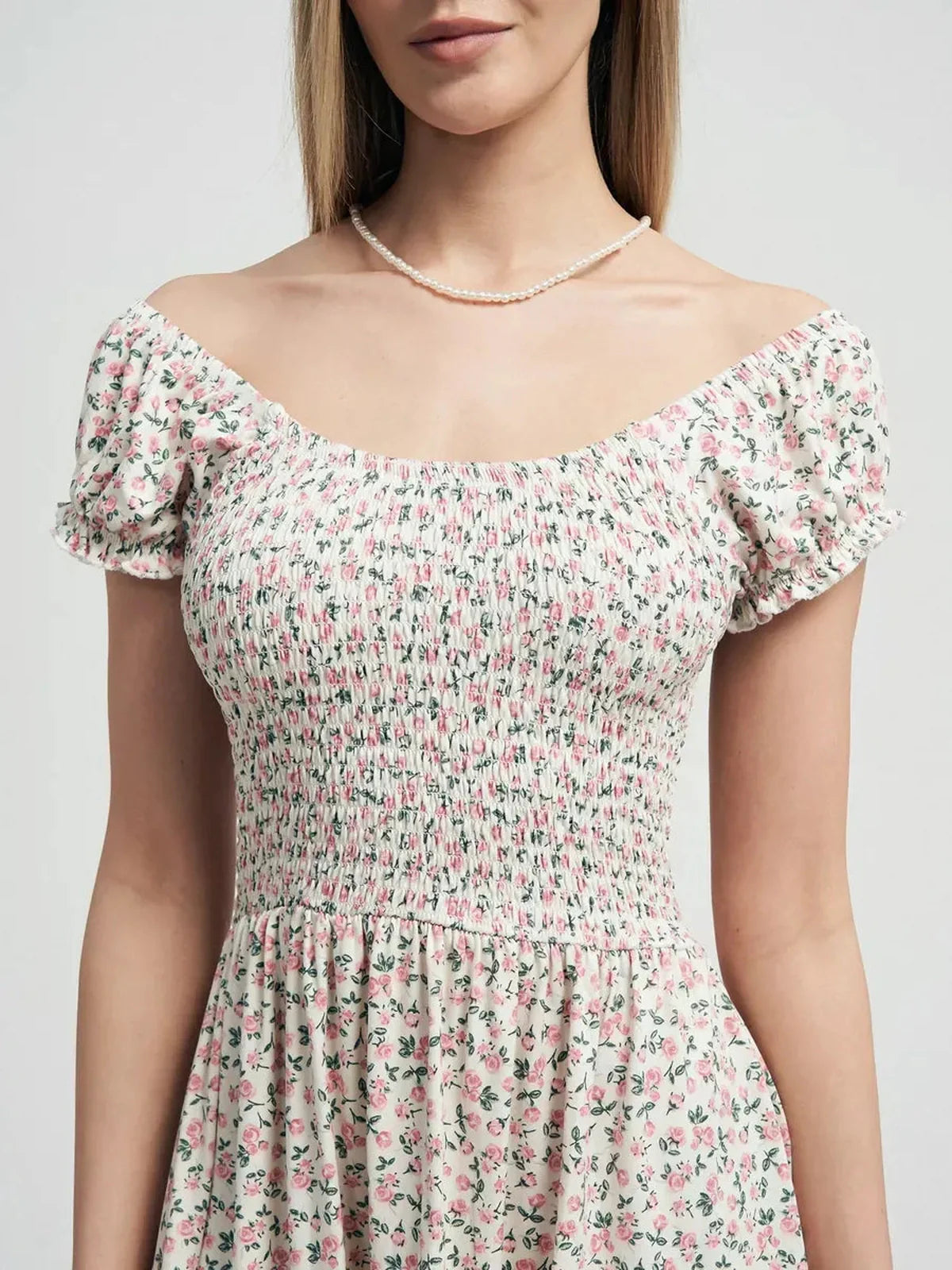 Close-up of a woman in a smocked, off-shoulder Blush Blossom dress featuring pink floral prints.