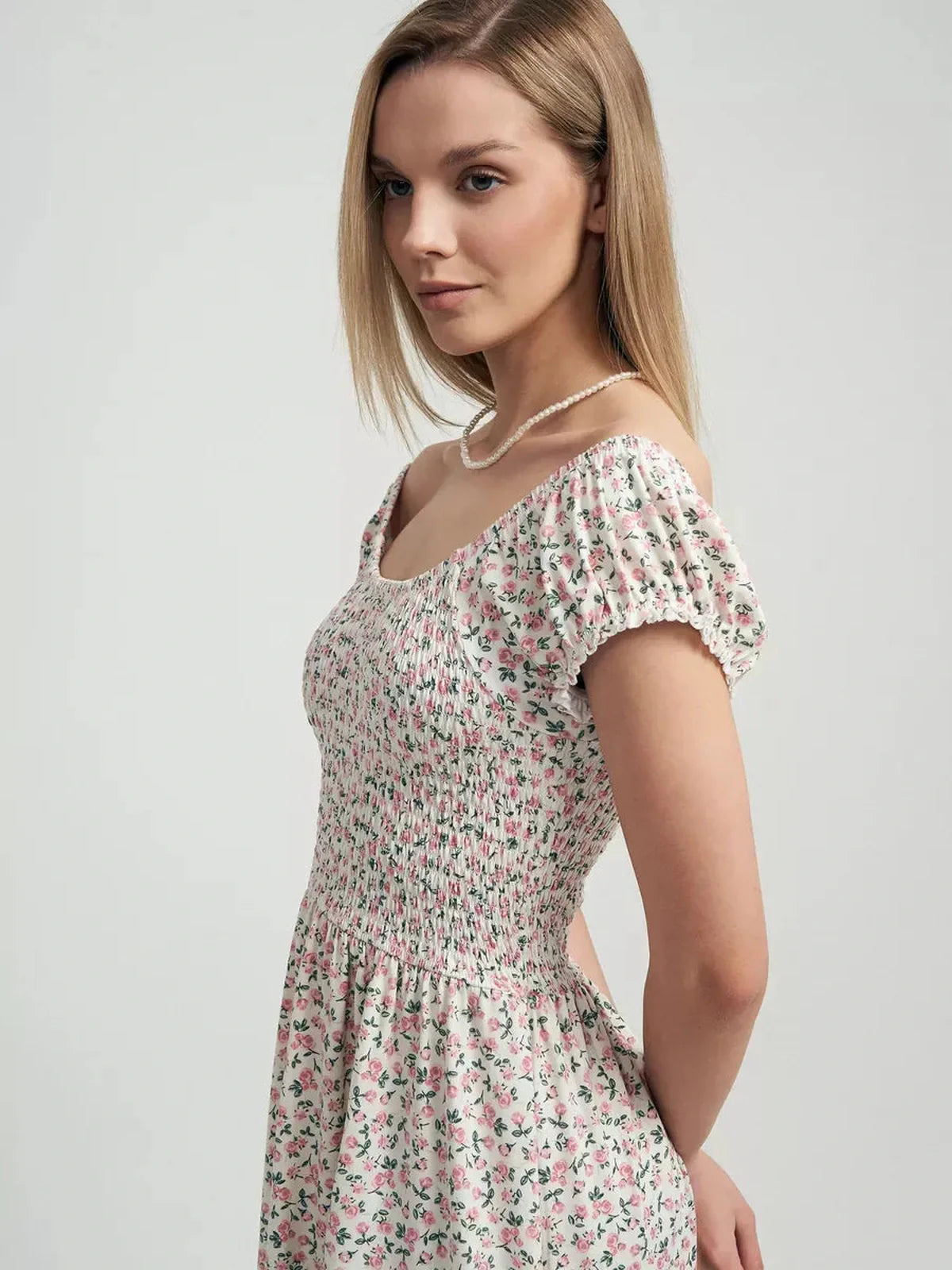 Side view of a woman in a blush floral summer dress with a smocked bodice and ruffled mini skirt, perfect for summer outings.