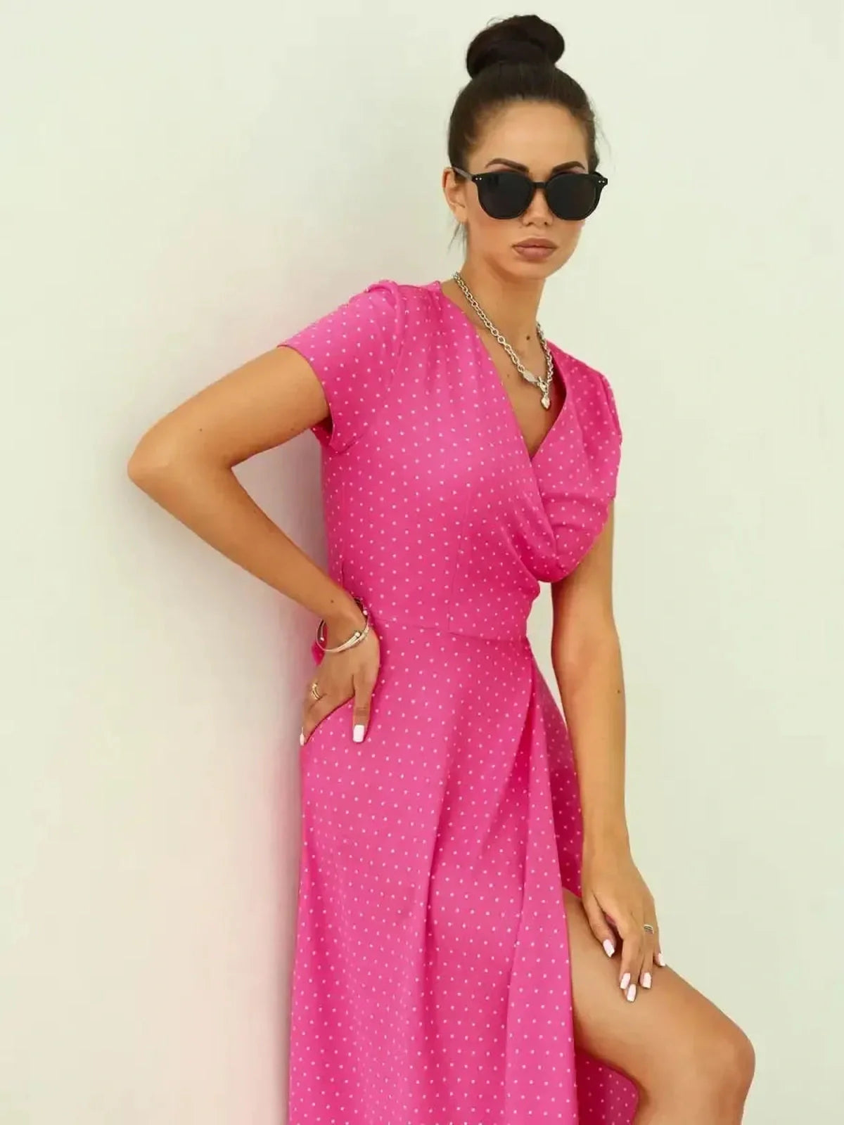 Woman in a vibrant pink polka dot Blush Radiance Maxi Dress, featuring a V-neckline and leg-baring slit.