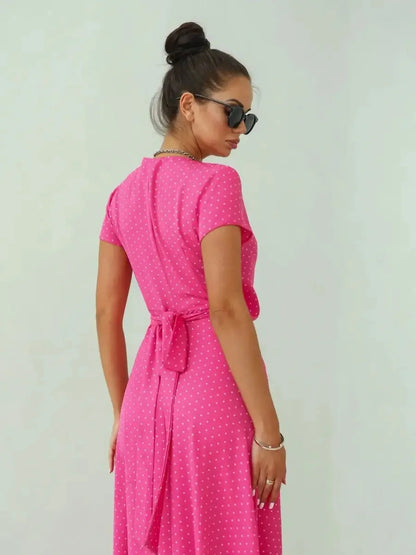 Woman in a pink polka dot maxi dress with short sleeves and a bow, showcasing a playful and feminine style.