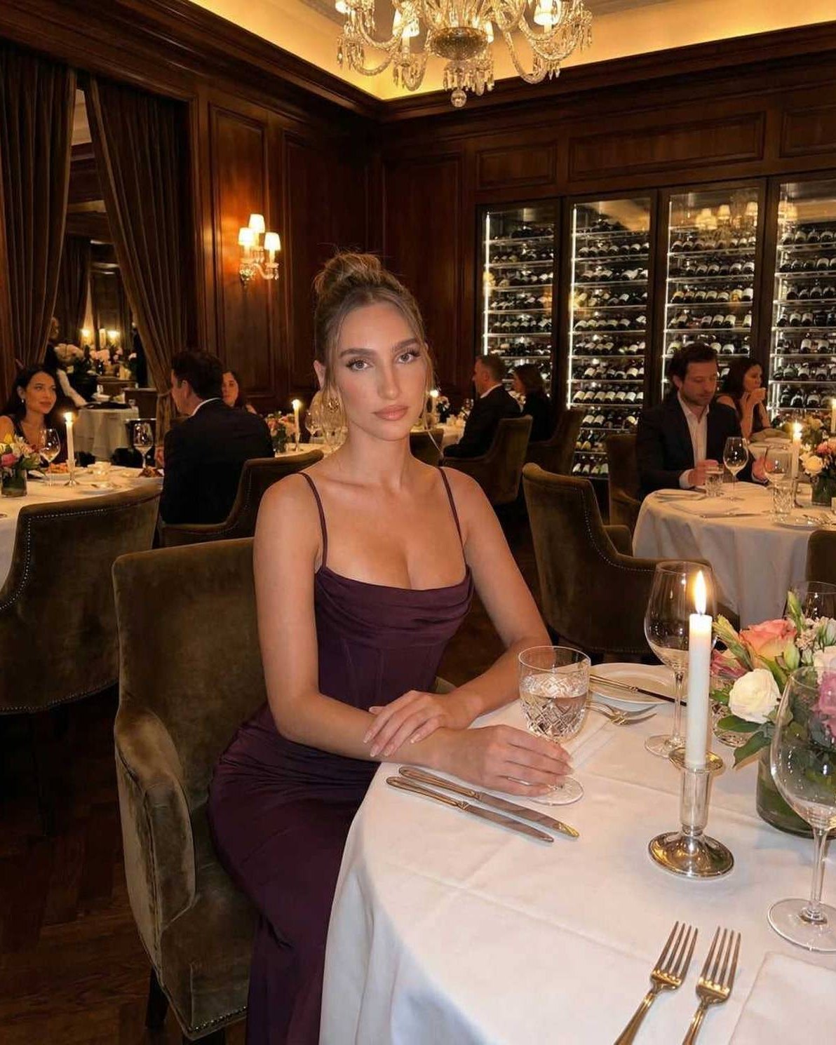 Celeste Maxi Dress worn at a refined dinner setting, featuring sleek sheath silhouette with spaghetti straps in deep plum color.